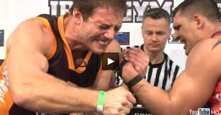 Zwei Athleten kämpfen im Armwrestling, während ein Schiedsrichter zuschaut.